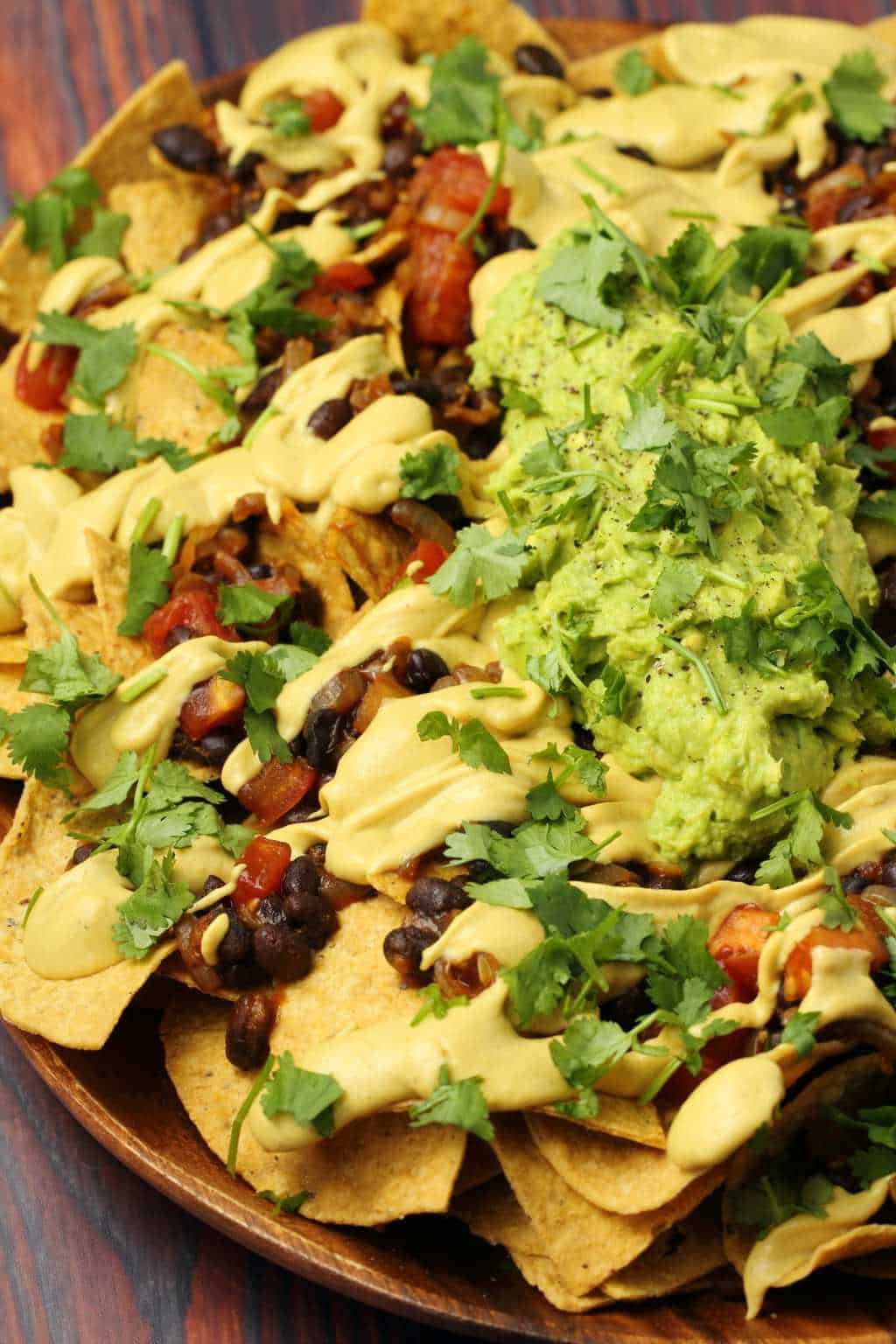 Vegan nacho cheese poured over fully loaded nachos with black beans, salsa and guacamole. 