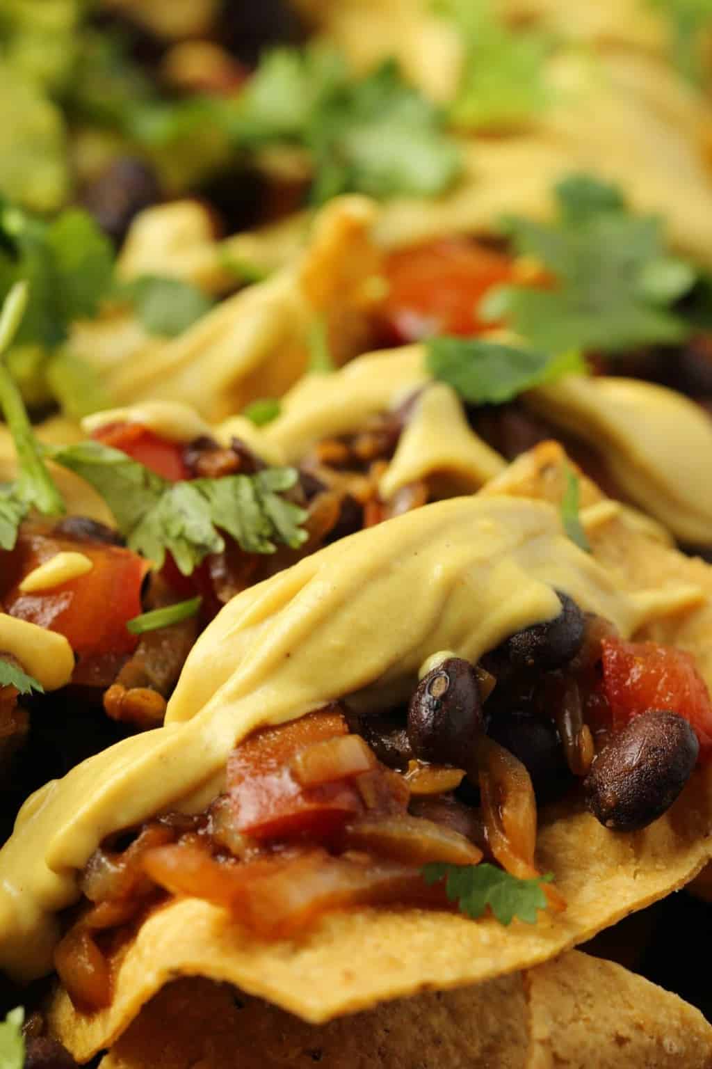 Vegan nacho cheese on top of fully loaded nachos with black beans, salsa and guacamole. 