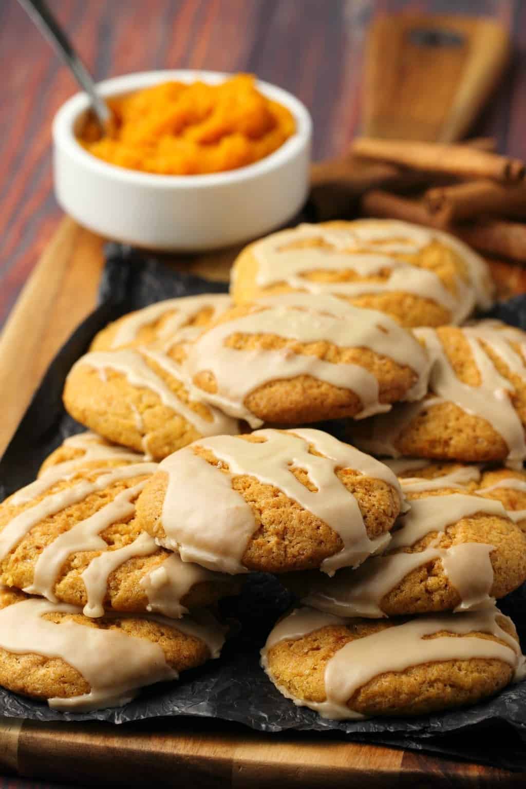 Vegan Pumpkin Cookies topped with maple glaze stacked up on a wooden board. 