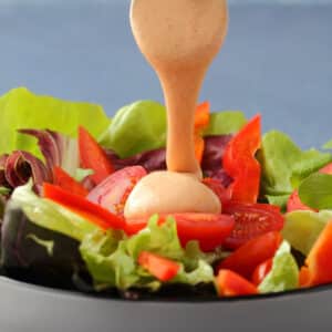 Vegan thousand island dressing drizzled off a spoon onto a salad.