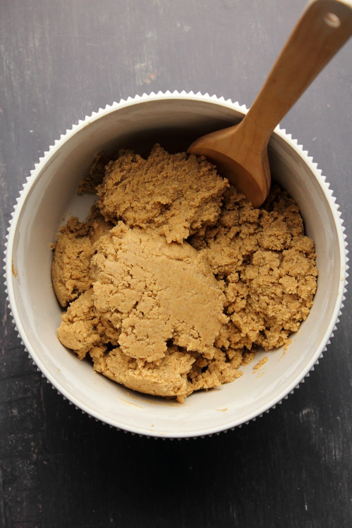Cookie dough for almond cookies in a white bowl with a wooden spoon. 