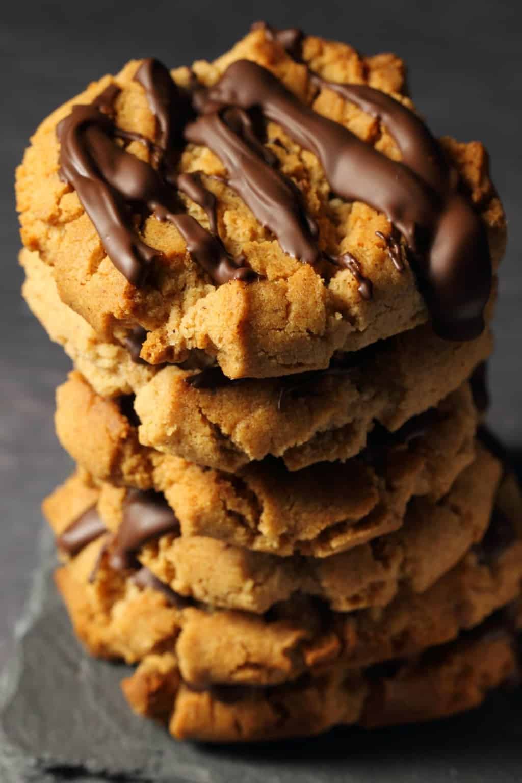 Vegan almond butter cookies drizzled with chocolate in a stack against a dark background. 