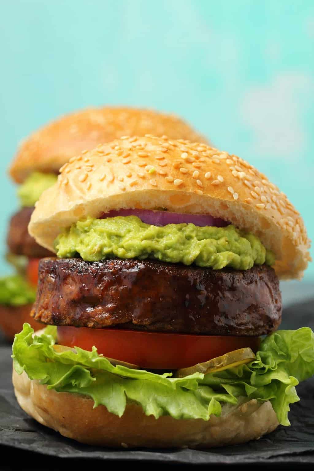 Vegan black bean burgers on burger buns with lettuce, pickles, tomato, guacamole and red onion. 