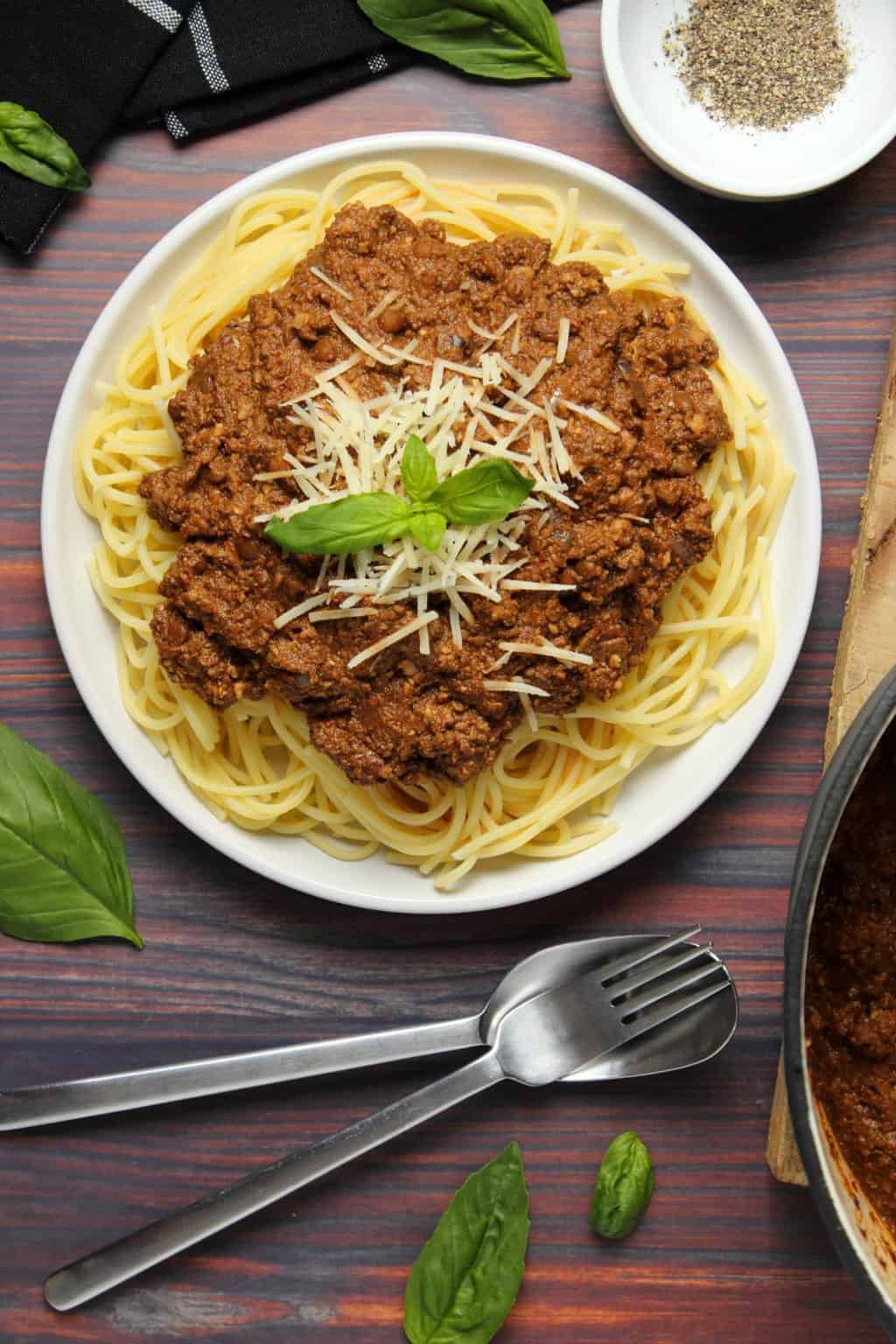 Vegan bolognese topped with fresh basil and vegan parmesan with spaghetti on a white plate. 