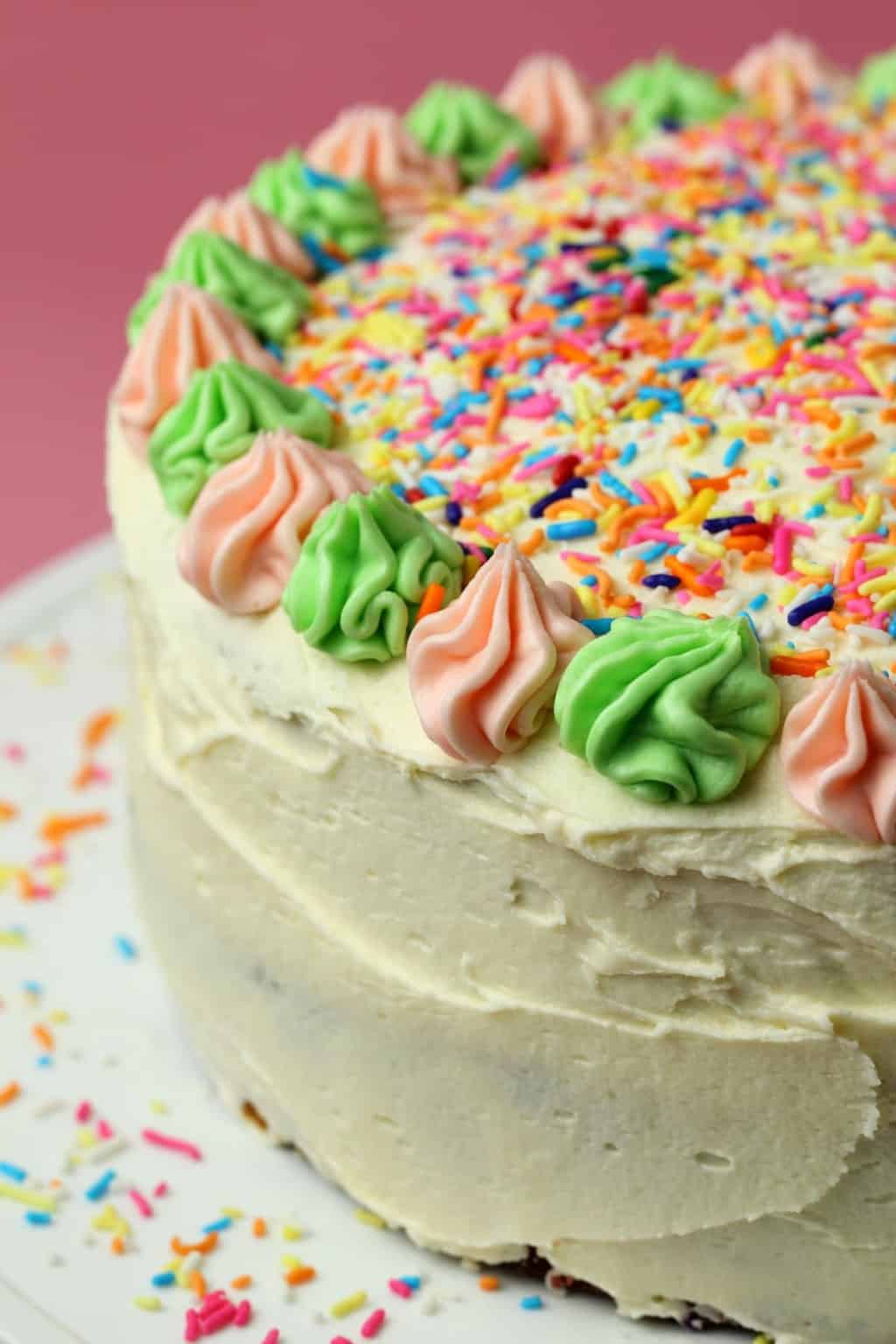 Vegan funfetti cake topped with sprinkles on a white cake stand. 