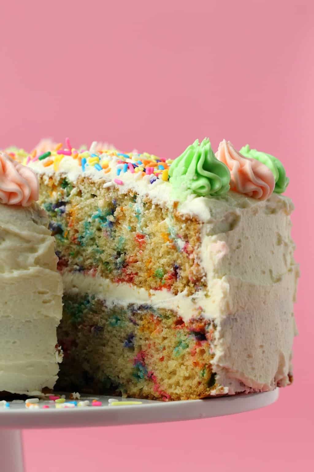 Vegan funfetti cake with one slice pulled out on a white cake stand. 