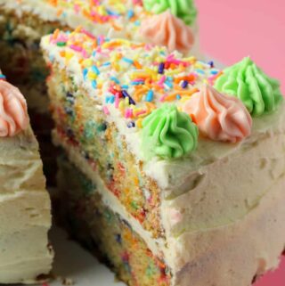 Vegan funfetti cake on a white cake stand with one slice cut and ready to serve