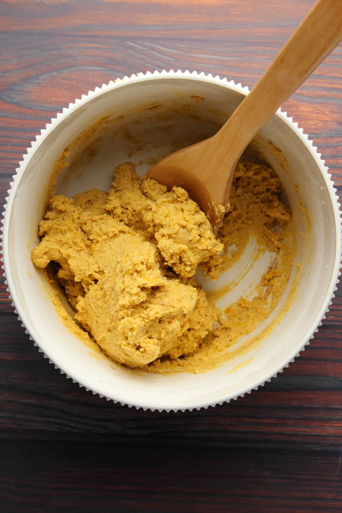Pumpkin cookie dough in a mixing bowl with a wooden spoon. 