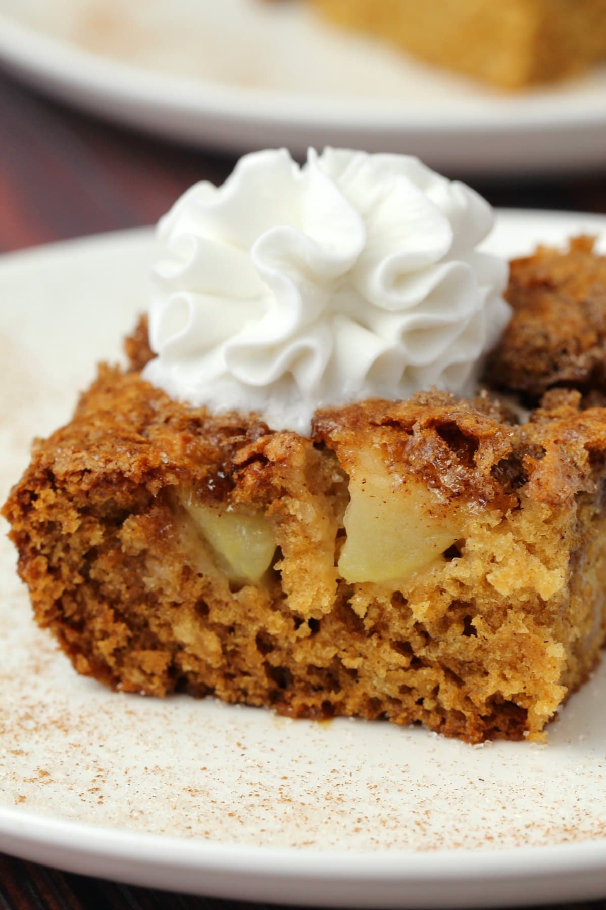 A slice of vegan apple cake topped with vegan whipped cream on a white plate. 