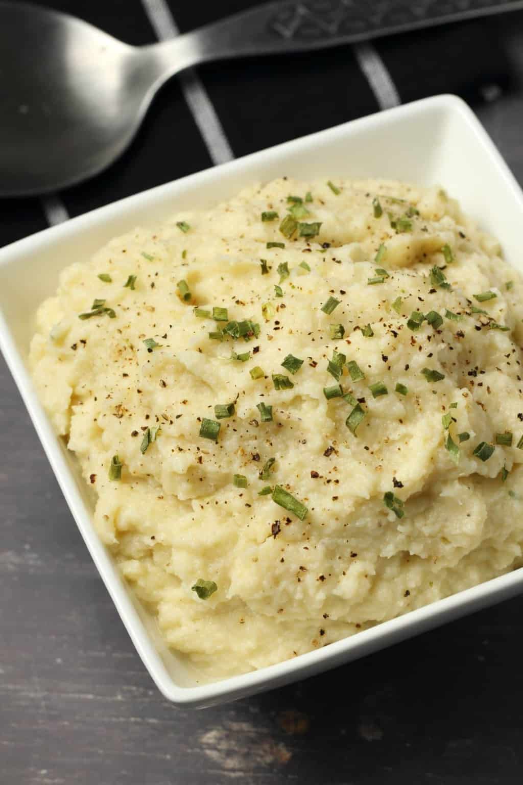 Vegan cauliflower mashed potatoes topped with chopped chives in a square white bowl. 