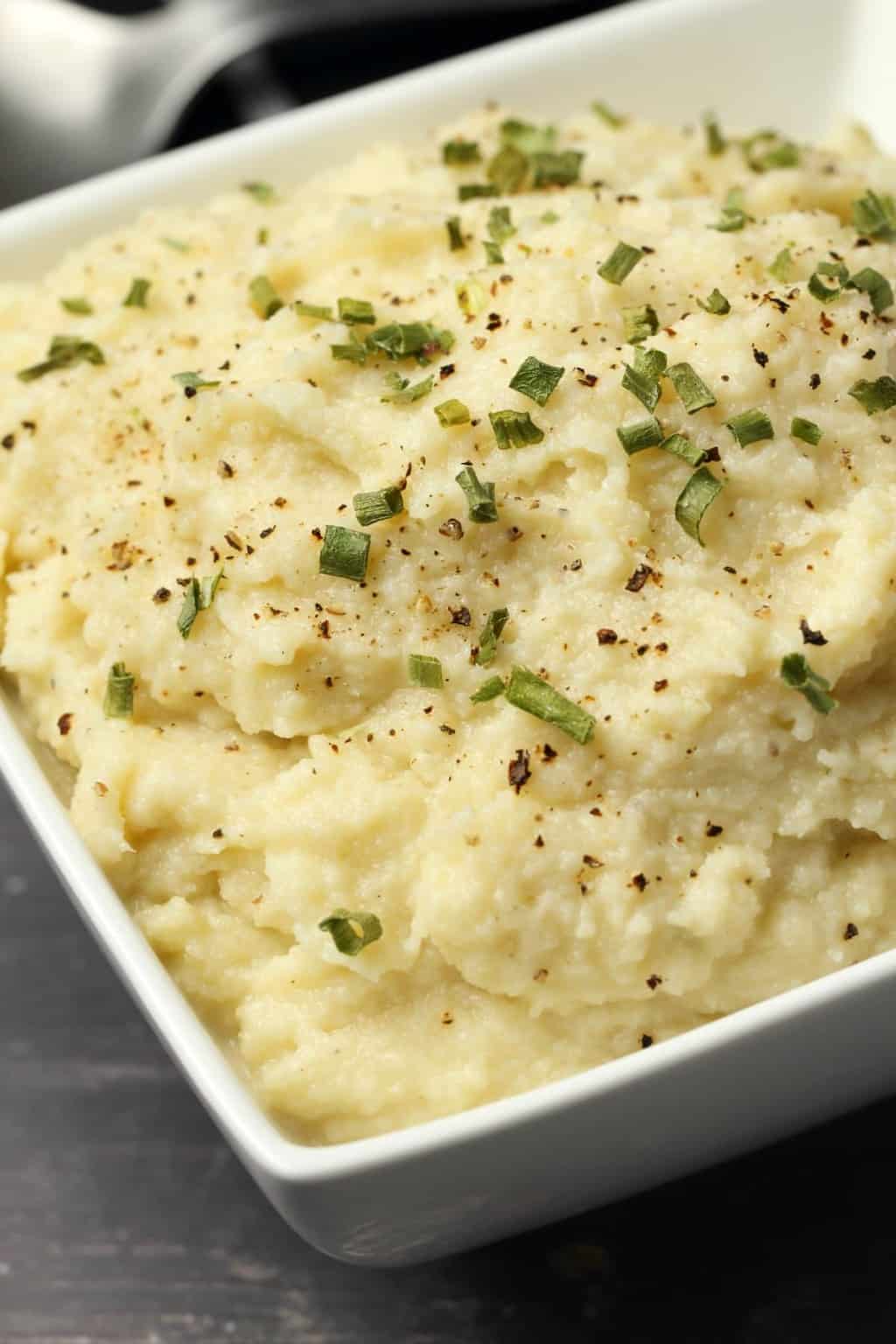 Vegan cauliflower mashed potatoes topped with chopped chives in a white bowl. 