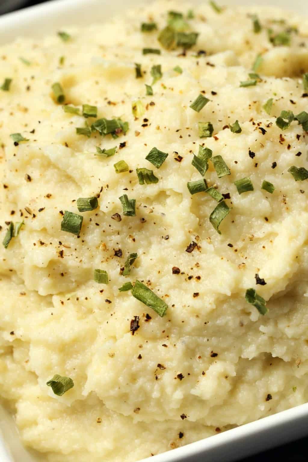 Vegan cauliflower mashed potatoes topped with chopped chives in a white bowl. 