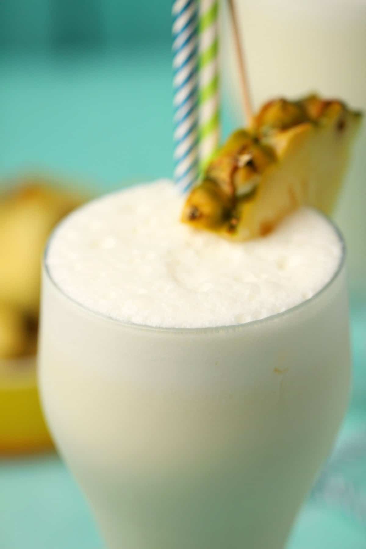 Vegan pina colada in a glass with a pineapple slice and straws. 