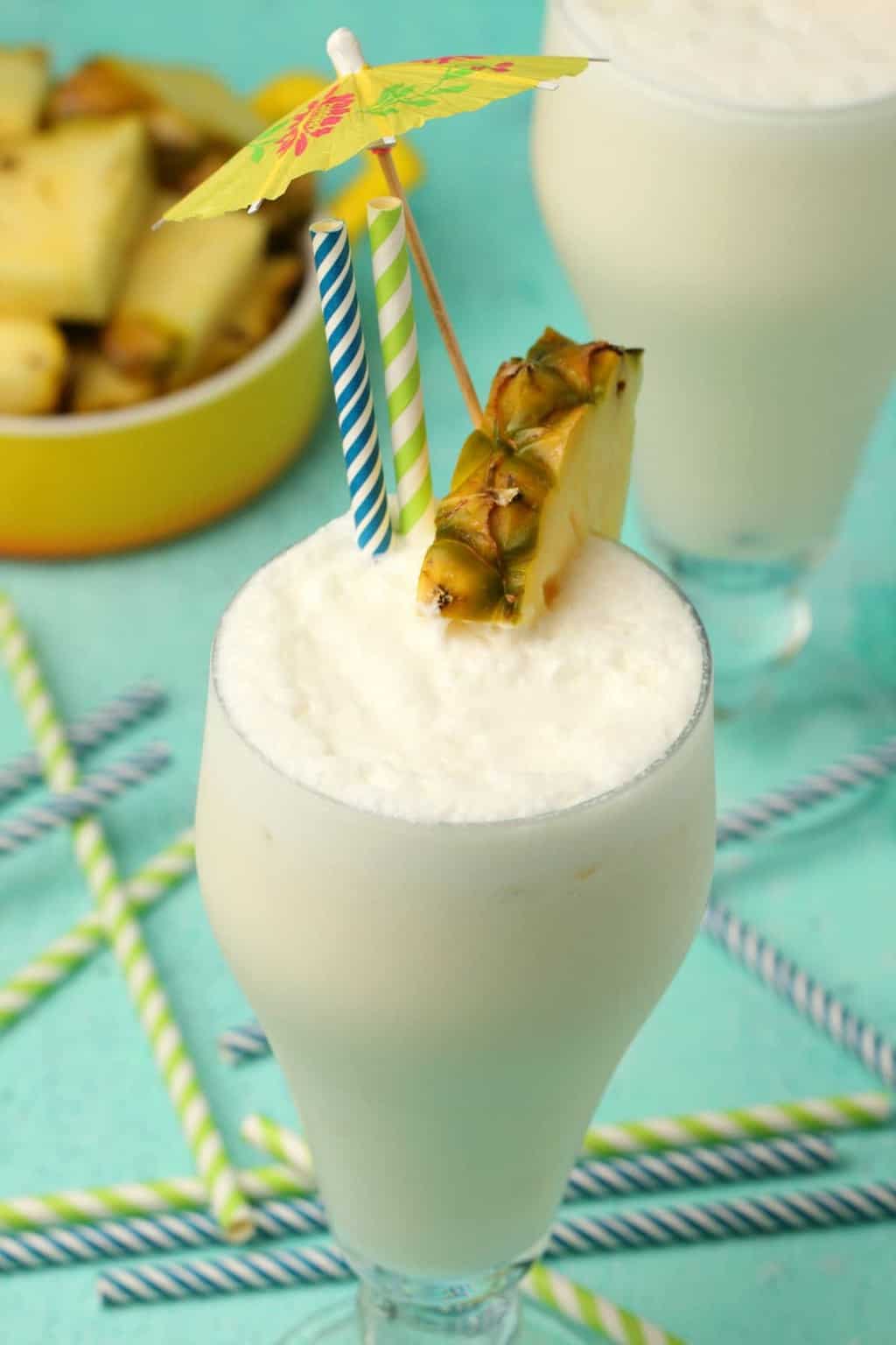 Vegan pina colada in a glass with a pineapple slice, straws and a cocktail umbrella.