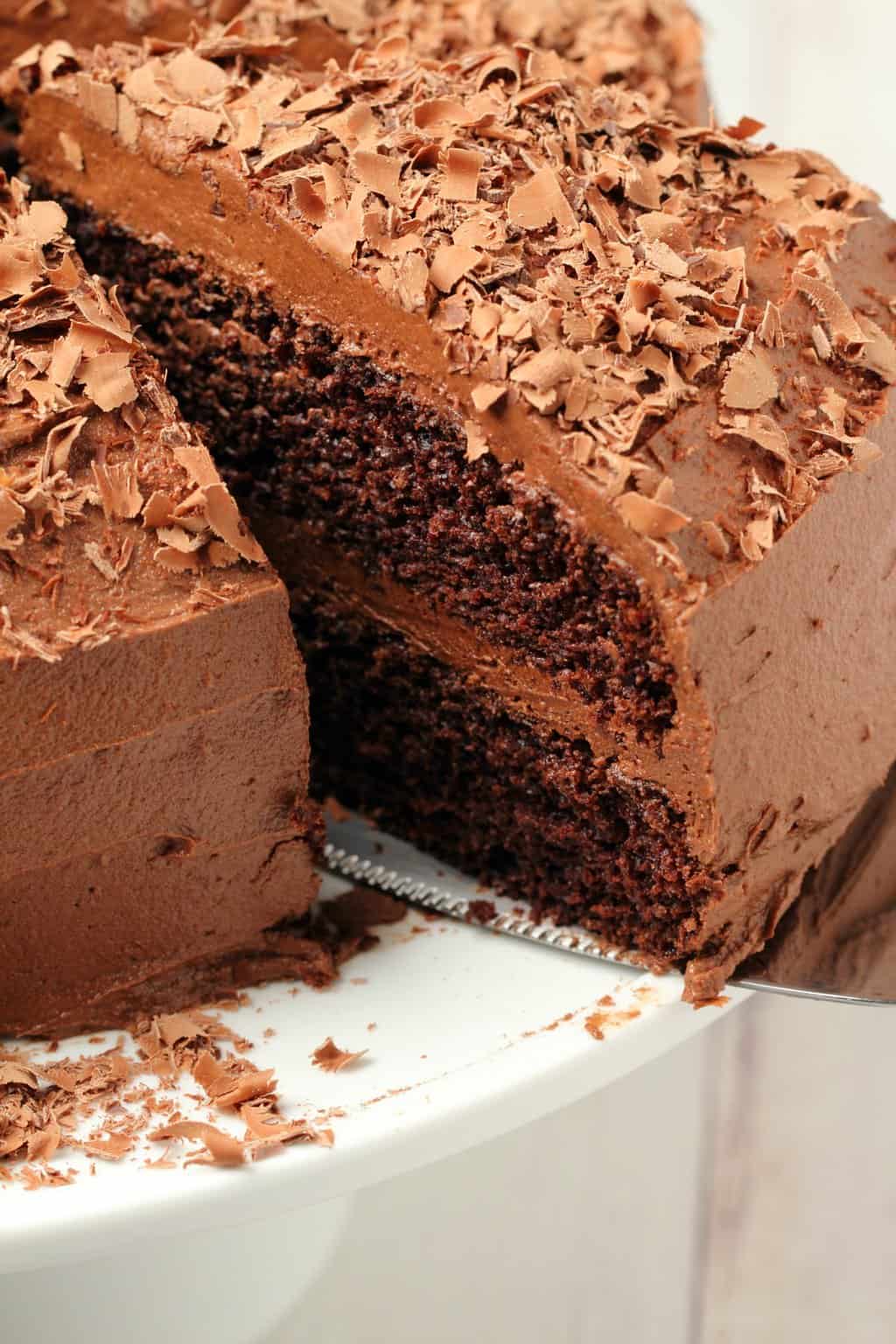 Chocolate cake with one slice cut and ready to serve on a white cake stand. 