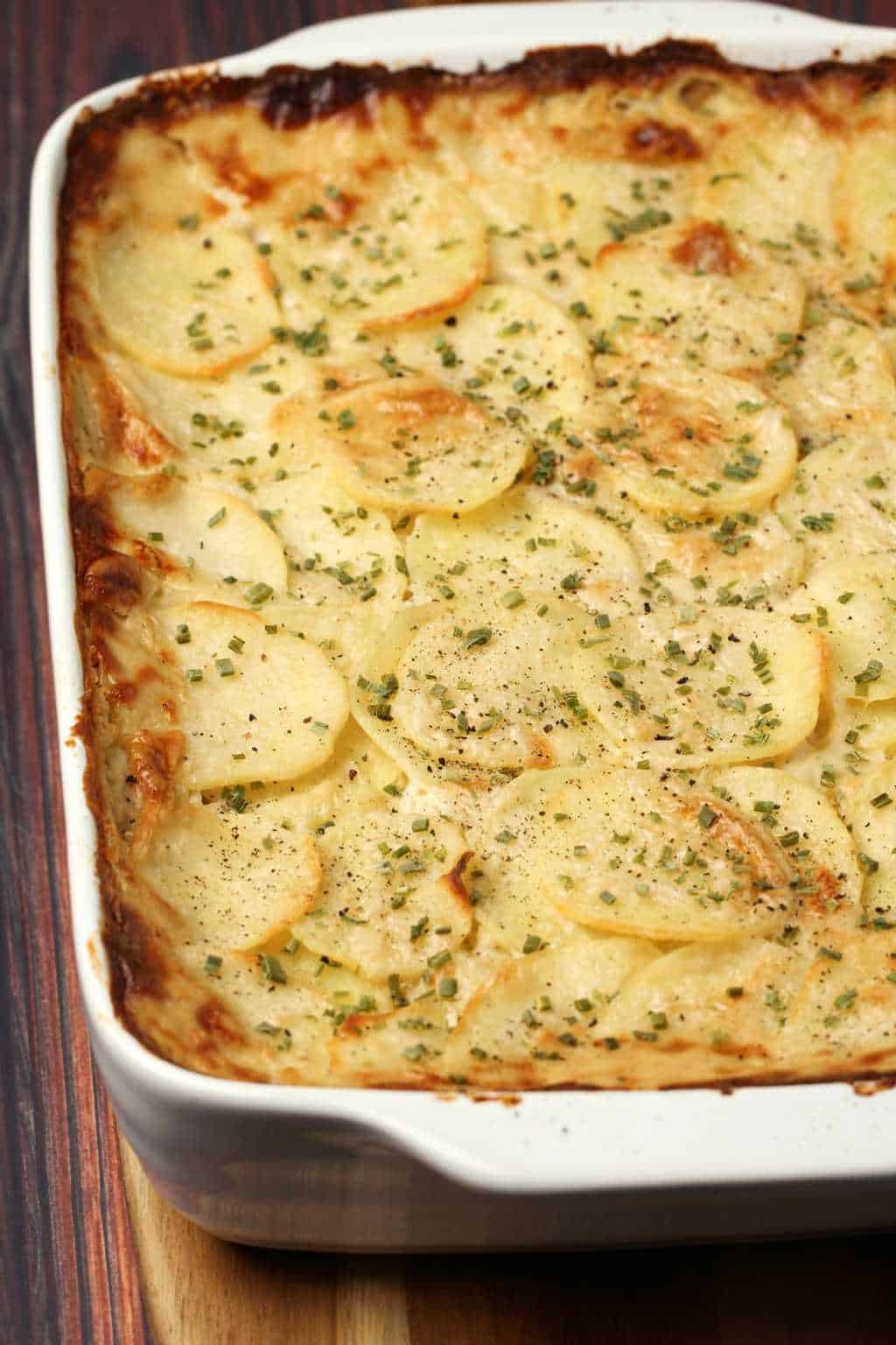 Vegan scalloped potatoes topped with chopped chives in a white dish. 