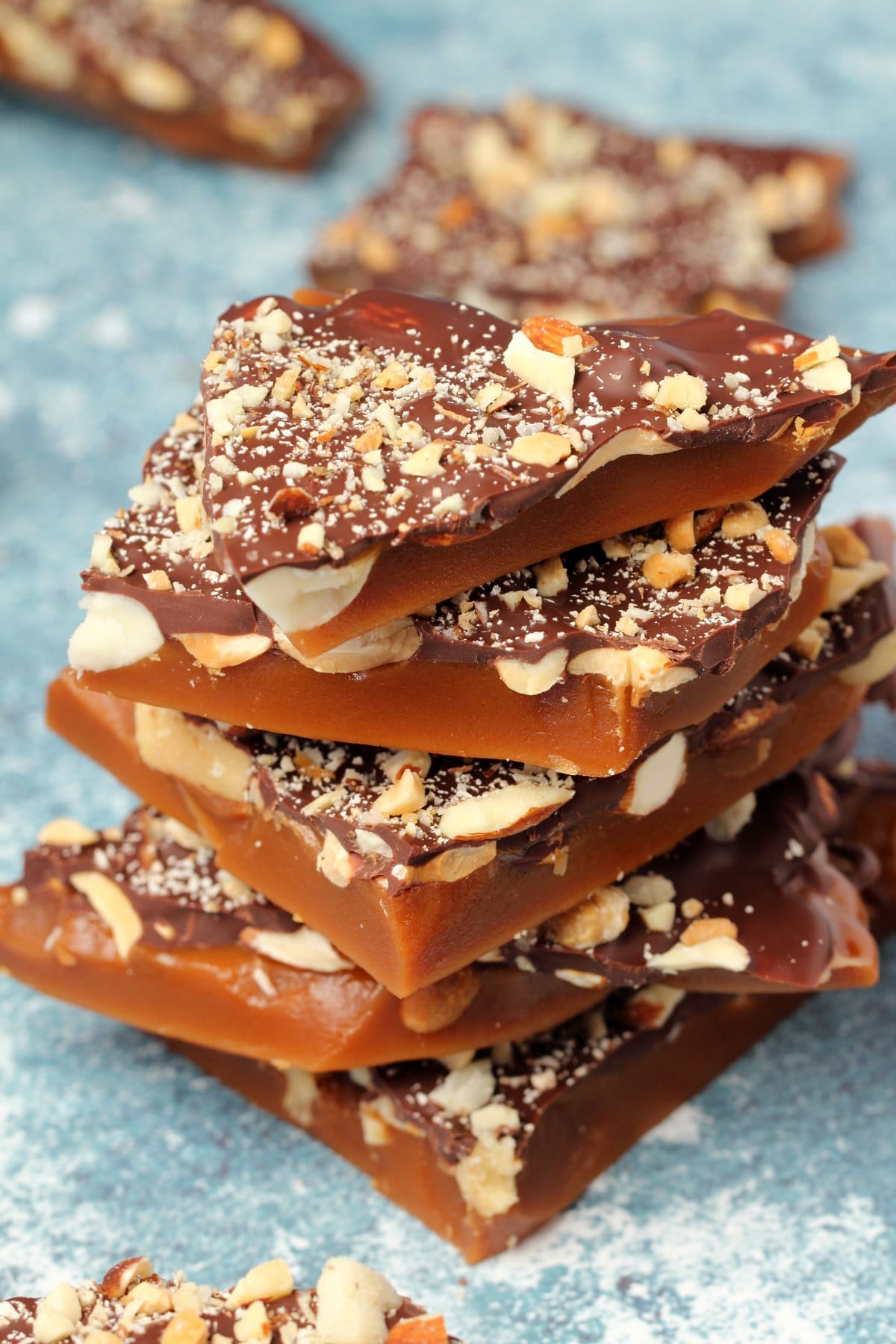 Vegan toffee topped with mixed nuts and melted chocolate in a stack. 