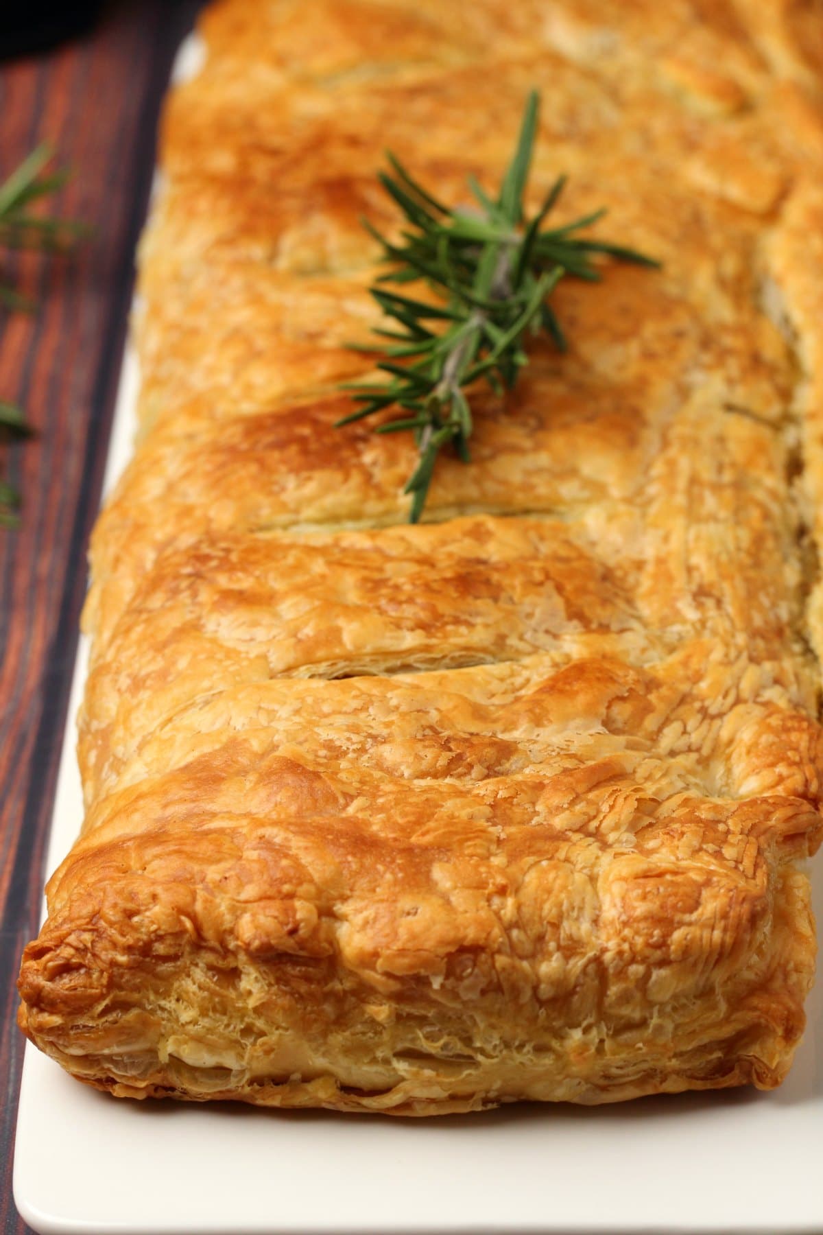 Vegan wellington topped with a sprig of fresh rosemary on a white plate. 