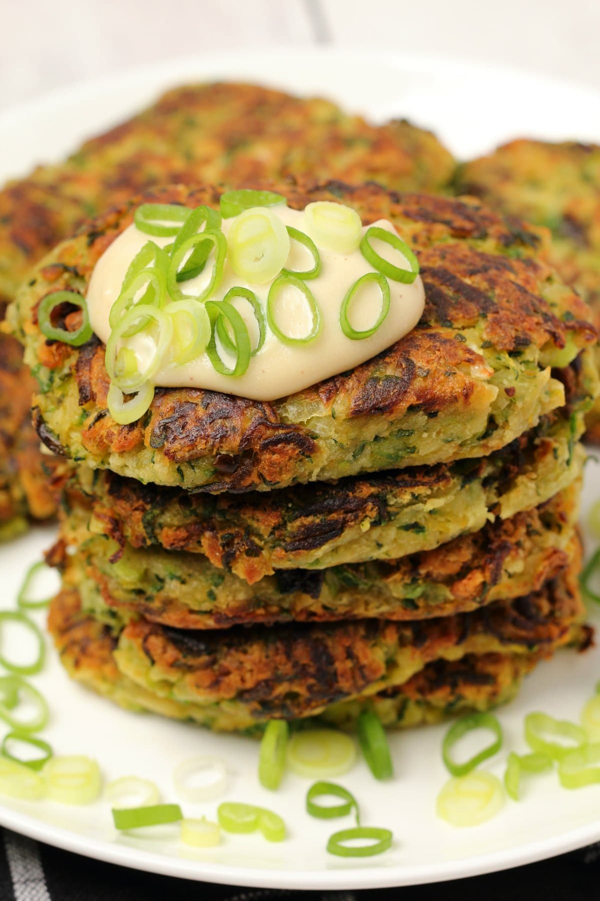Vegan zucchini fritters topped with vegan sour cream and chopped spring onions on a white plate. 