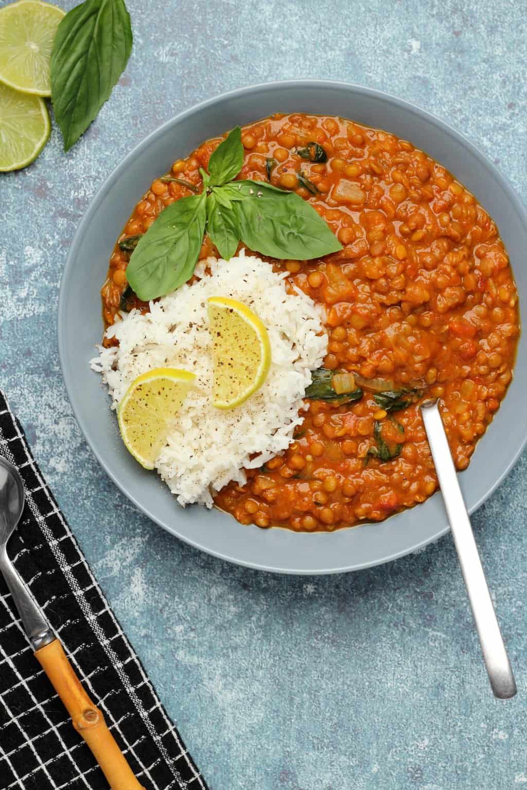 Vegan lentil curry with basmati rice and fresh basil in a blue bowl. 