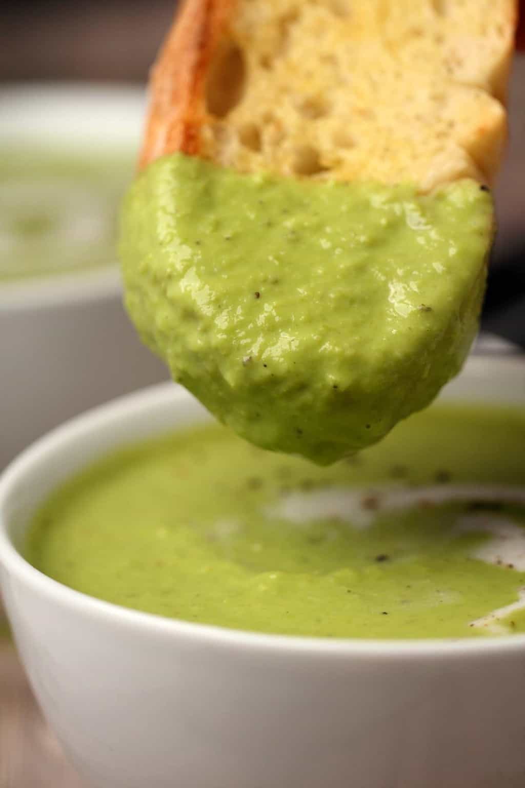 Slice of bread dipping into a bowl of vegan pea soup. 