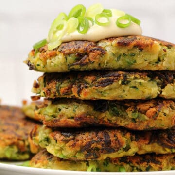Vegan zucchini fritters stacked up on a white plate.