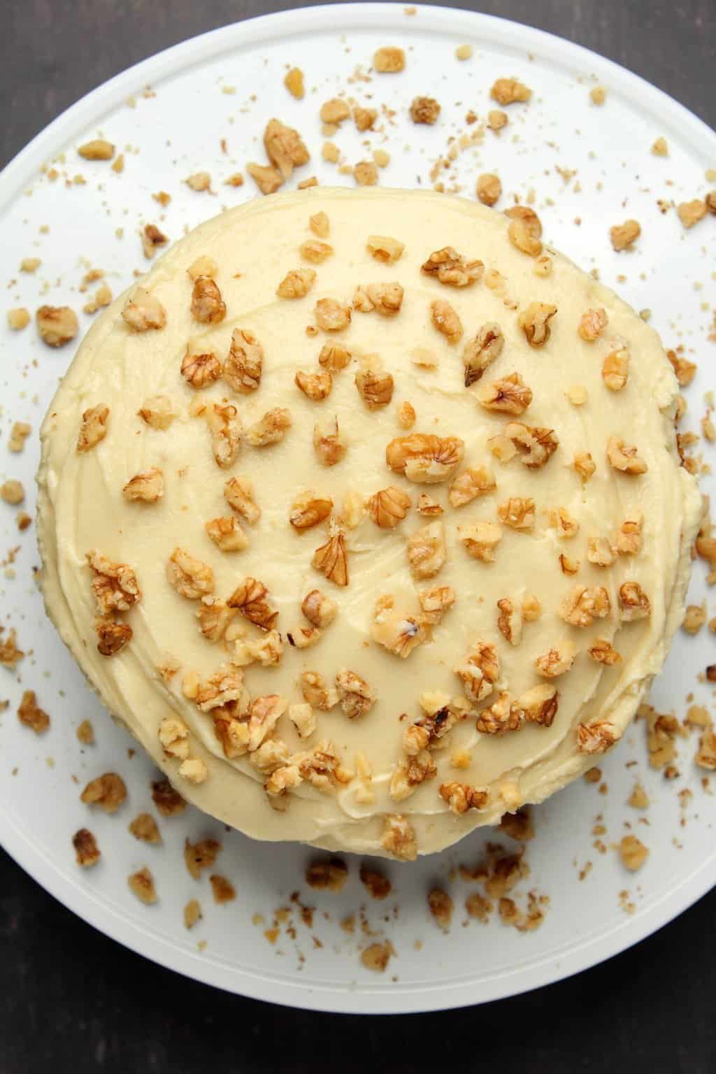 Vegan cream cheese frosting topped with crushed walnuts on a carrot cake. 