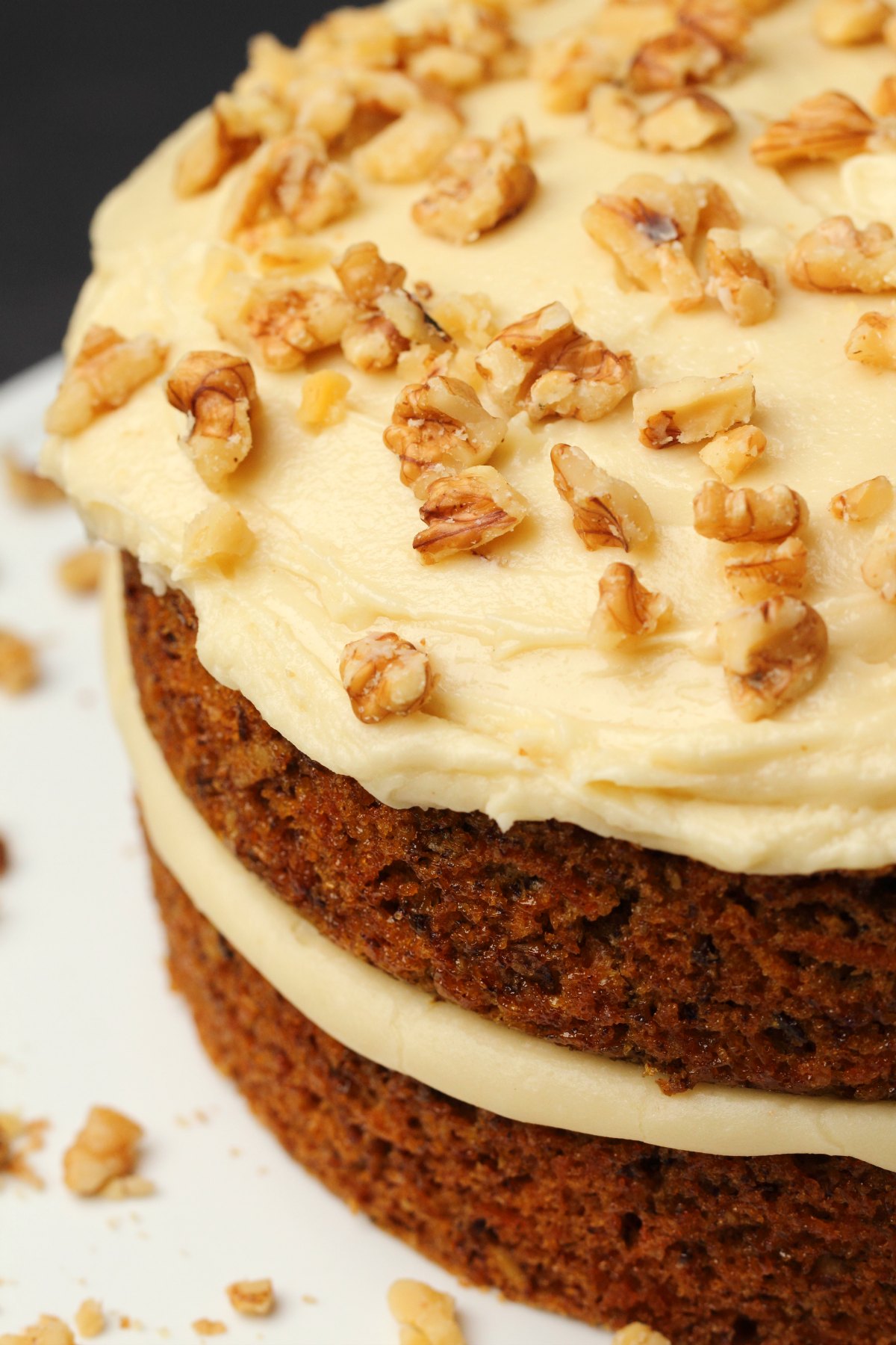 Vegan cream cheese frosting topped with crushed walnuts on a carrot cake. 
