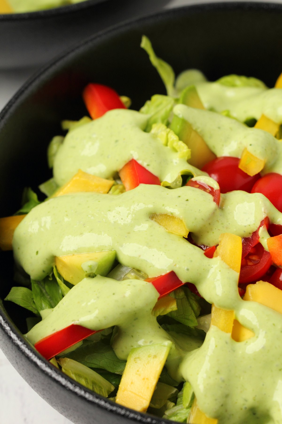 Vegan green goddess dressing drizzled over salad in a black bowl. 