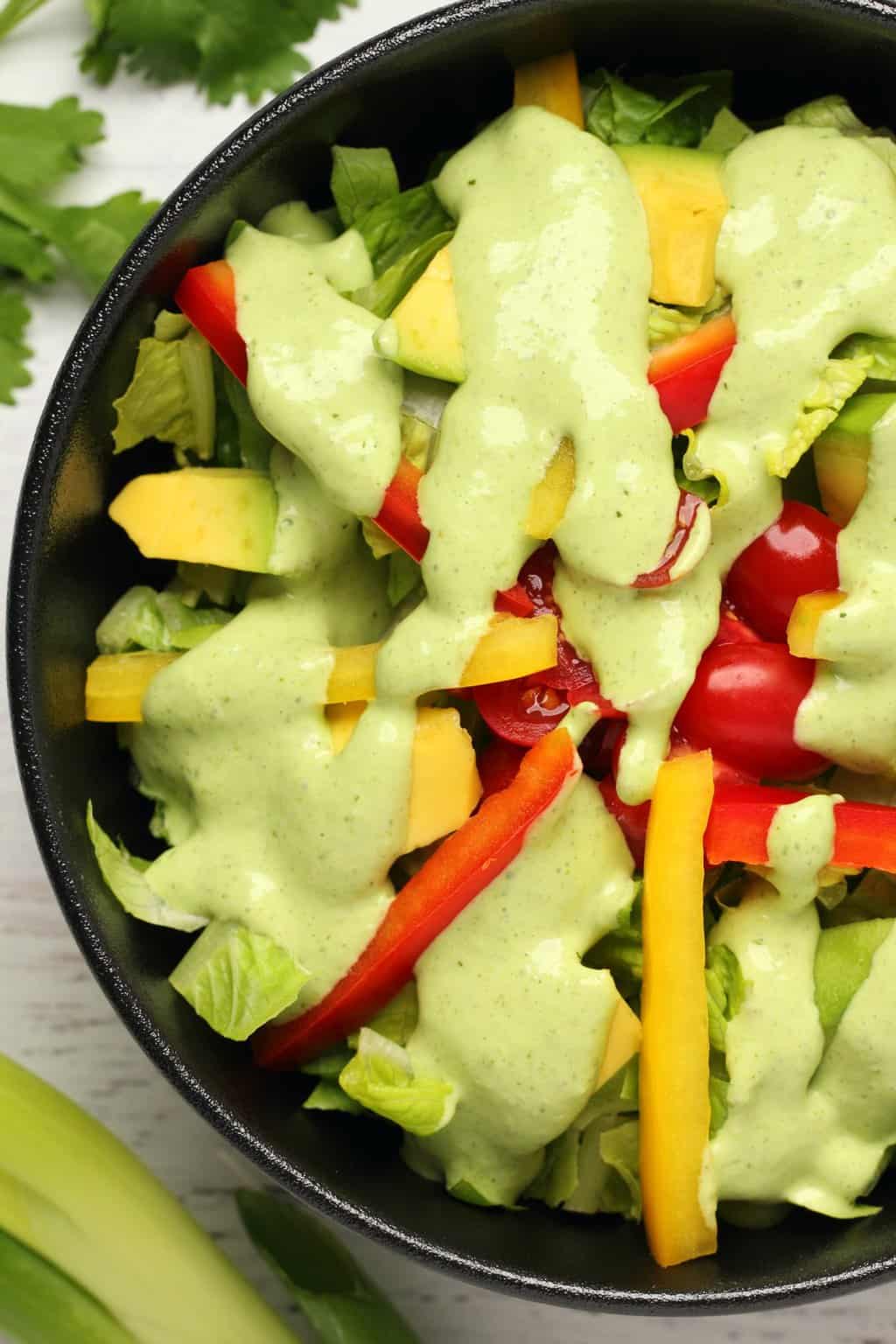 Vegan green goddess dressing drizzled over a salad in a black bowl. 