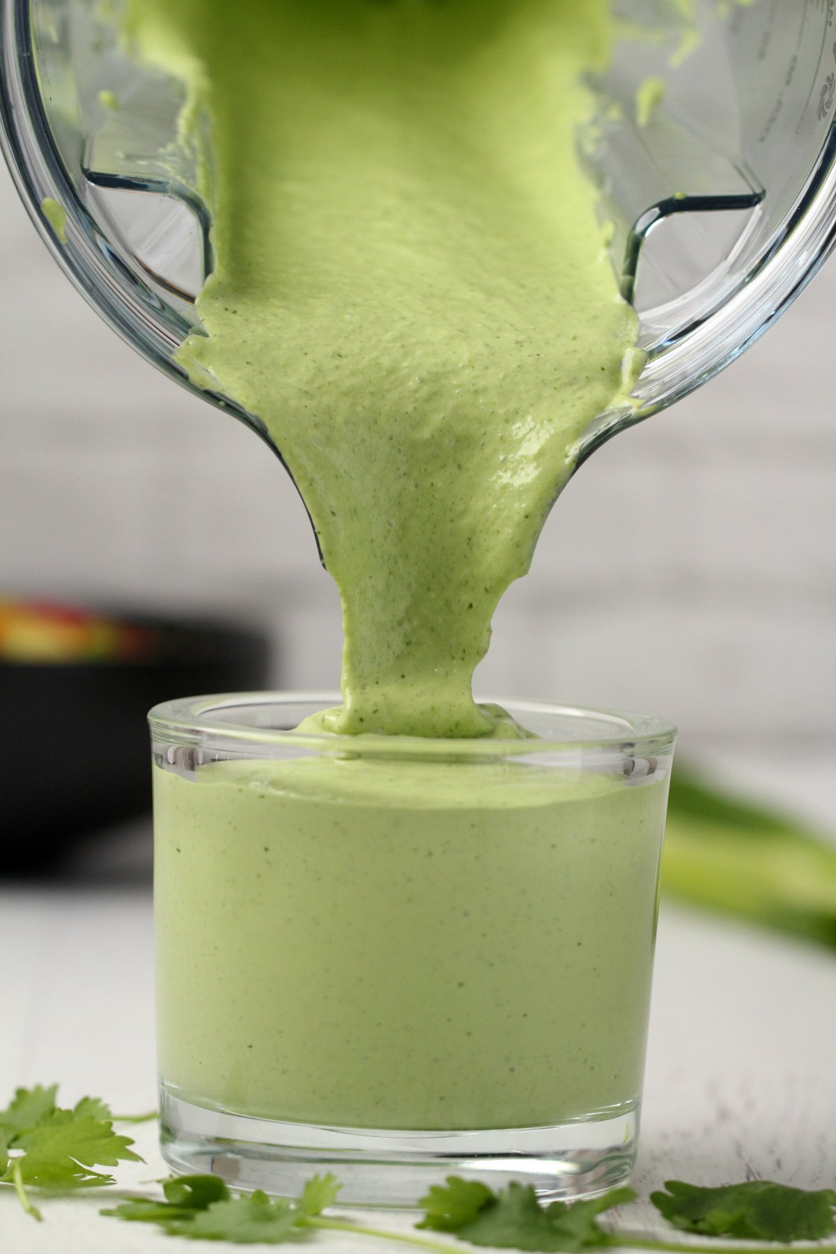 Vegan green goddess dressing pouring from a blender jug into a glass jar. 