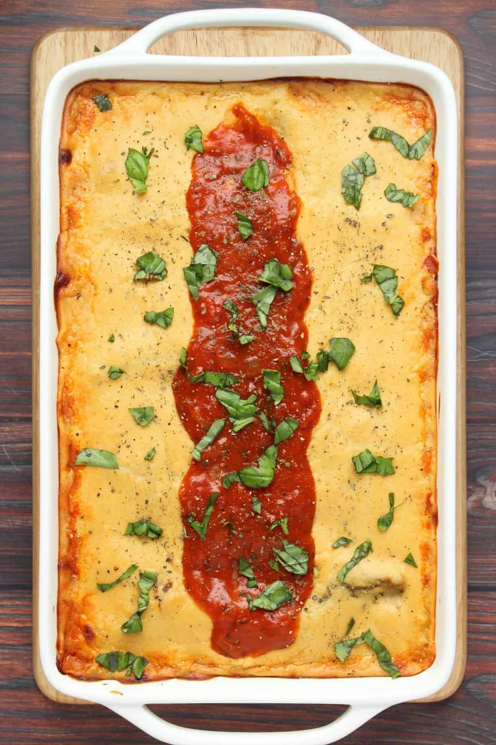 Freshly baked vegan lasagna decorated with marinara sauce and fresh chopped basil in a white dish. 