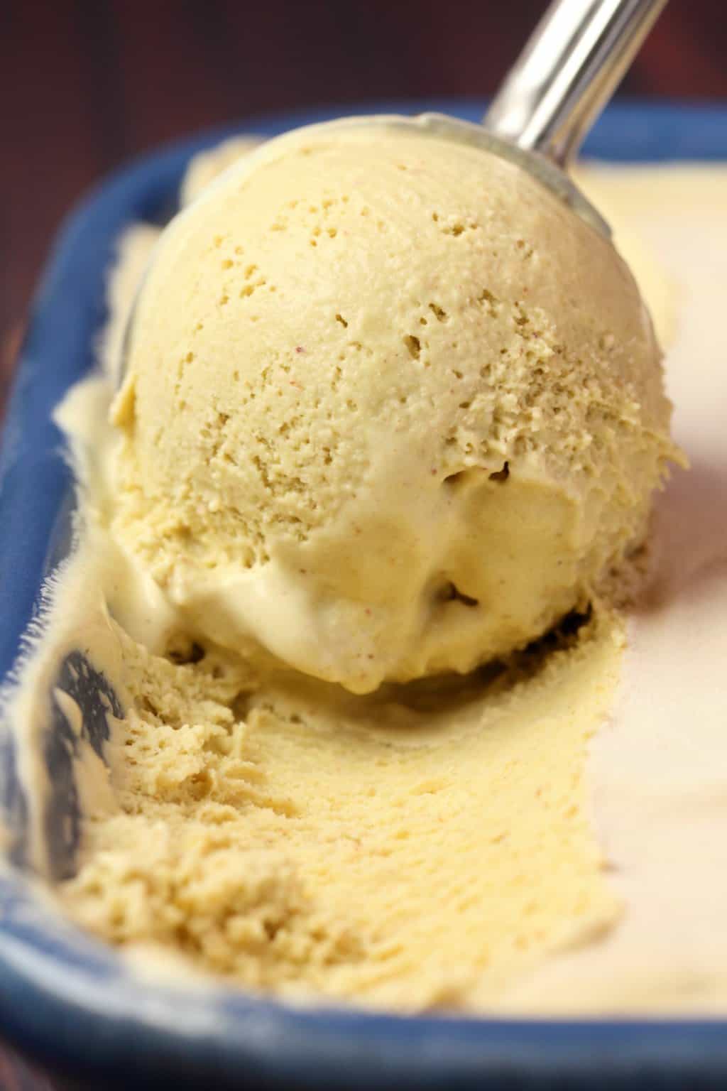 Vegan pistachio ice cream in a blue ceramic loaf pan with an ice cream scoop. 