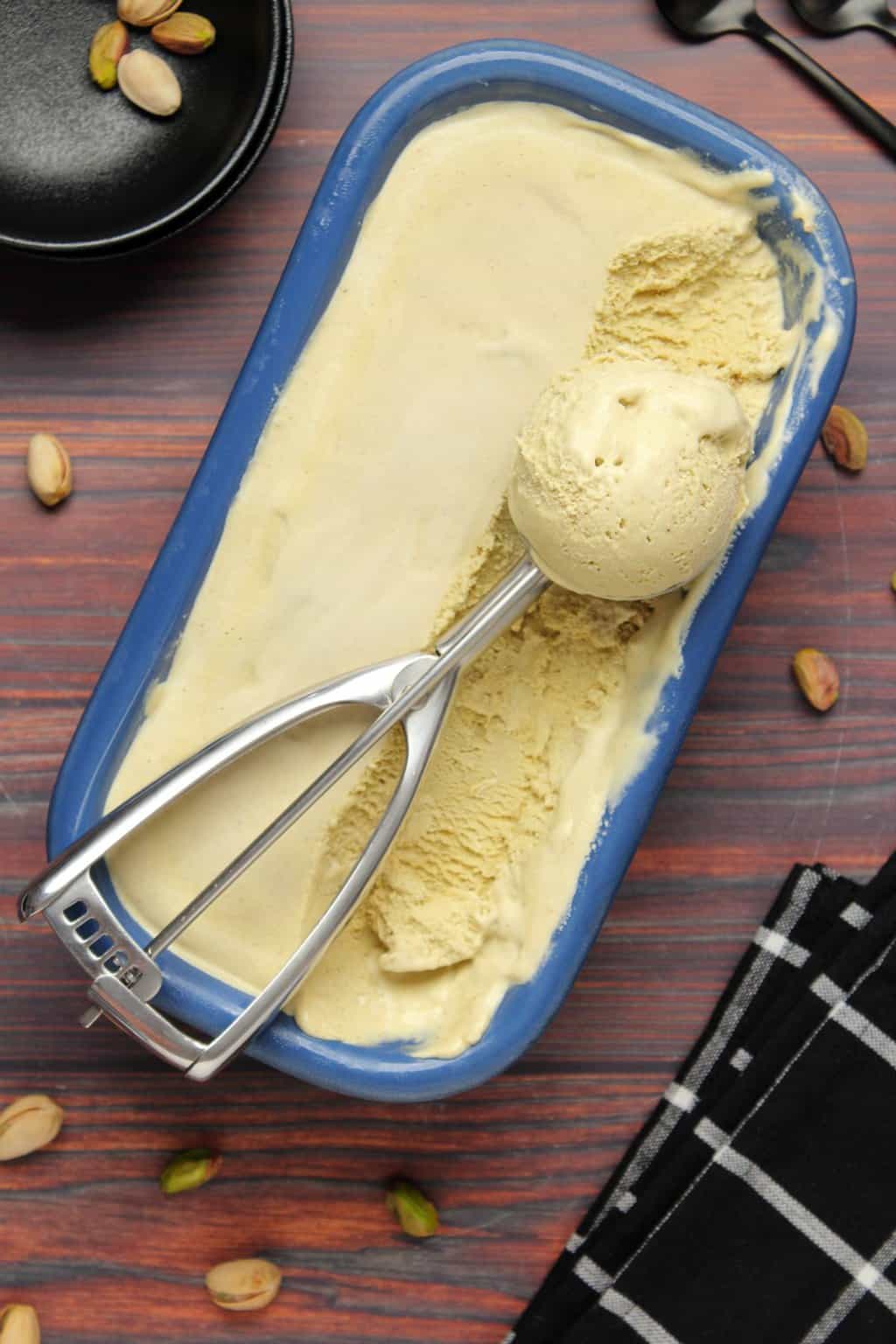 Vegan pistachio ice cream in a blue ceramic loaf pan with an ice cream scoop. 