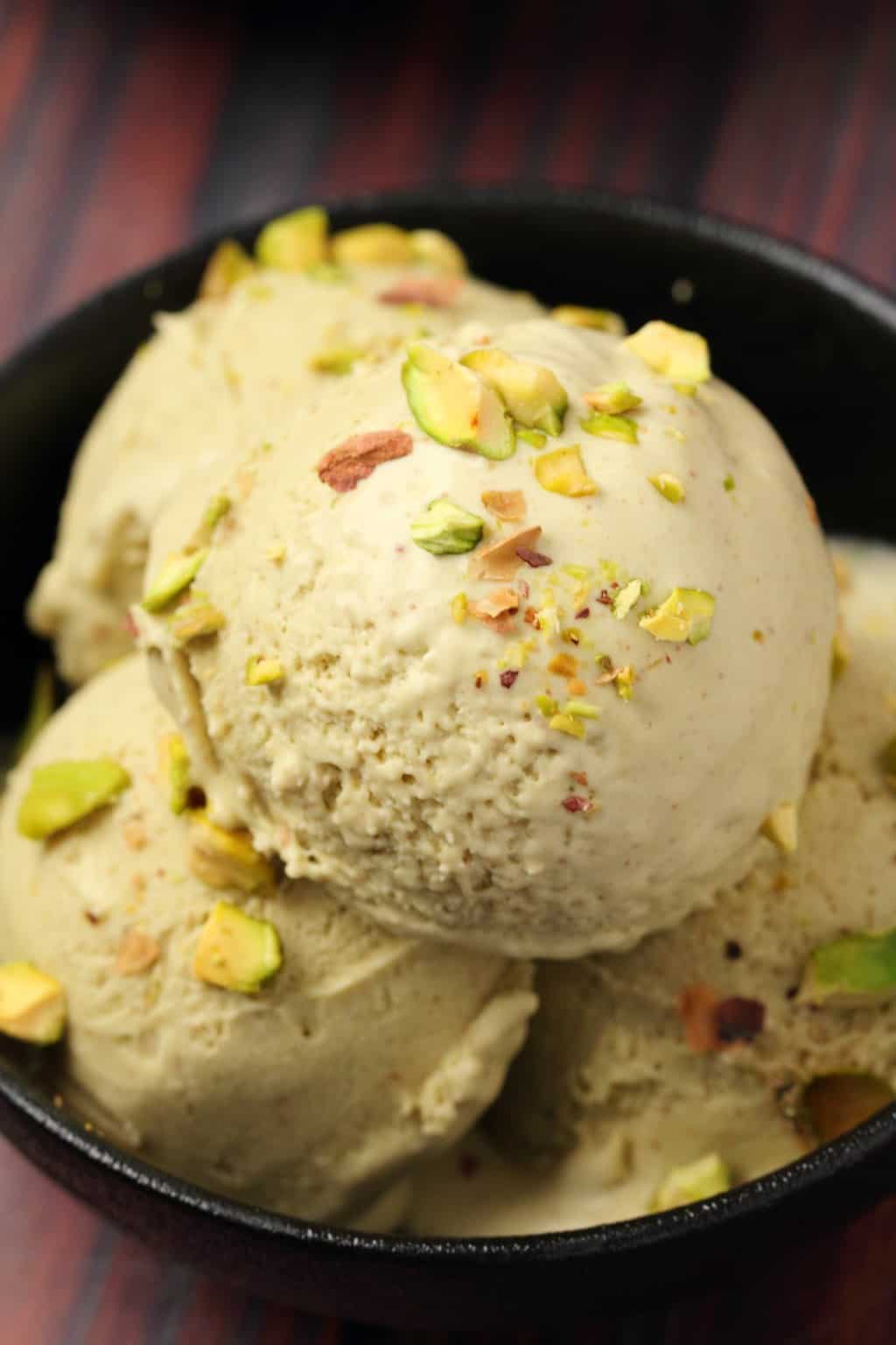 Vegan pistachio ice cream topped with crushed pistachios in a black bowl. 