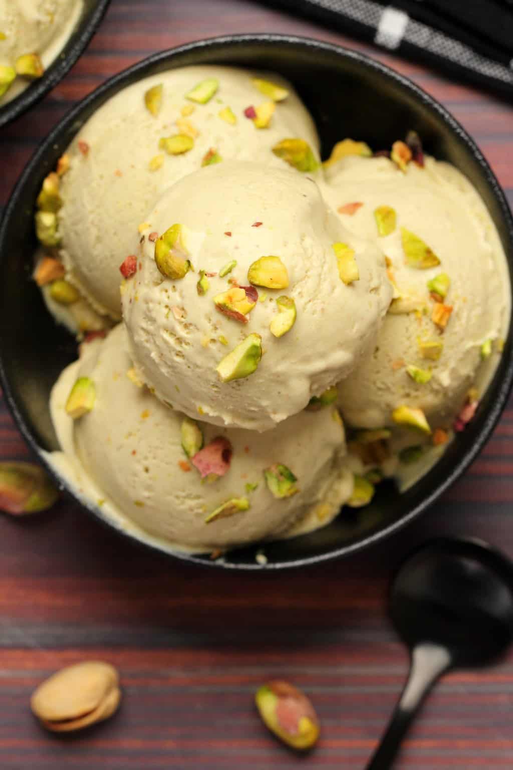 Vegan pistachio ice cream topped with crushed pistachios in a black bowl. 