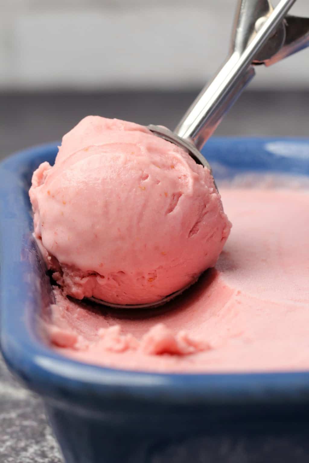 Vegan strawberry ice cream in a blue ceramic loaf pan with an ice cream scoop. 