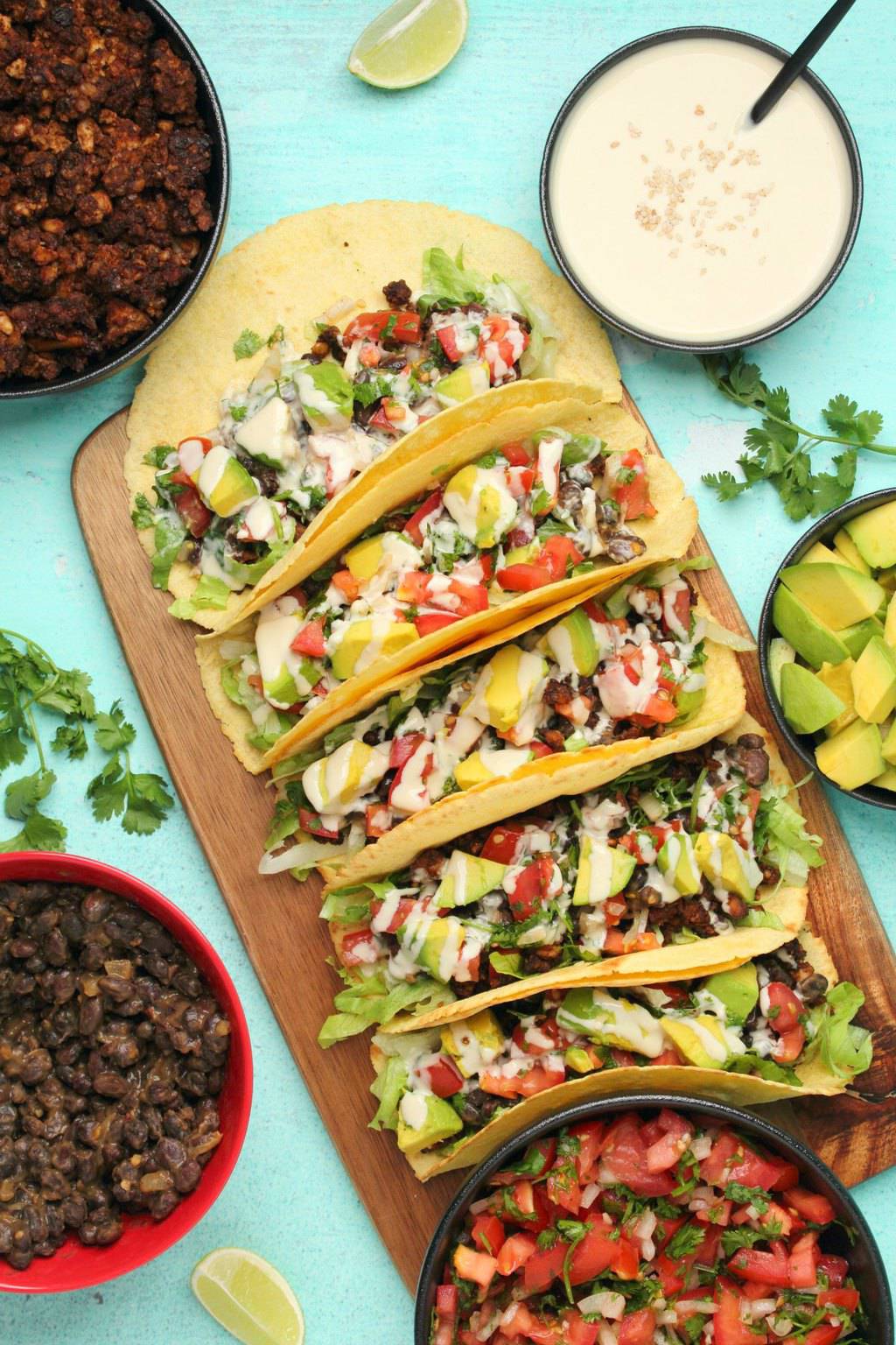 Vegan tacos with black beans, vegan taco meat, pico de gallo, avocado and tahini sauce on a wooden board. 