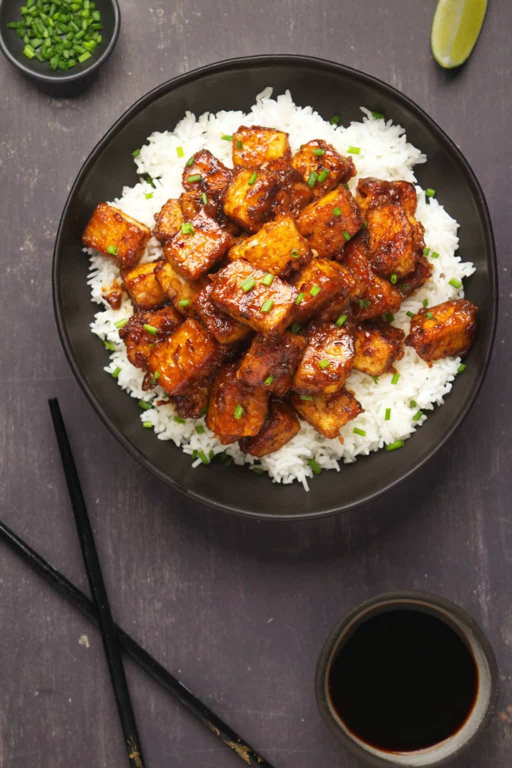 General Tso's tofu served with basmati rice and chopped chives in a black bowl. 