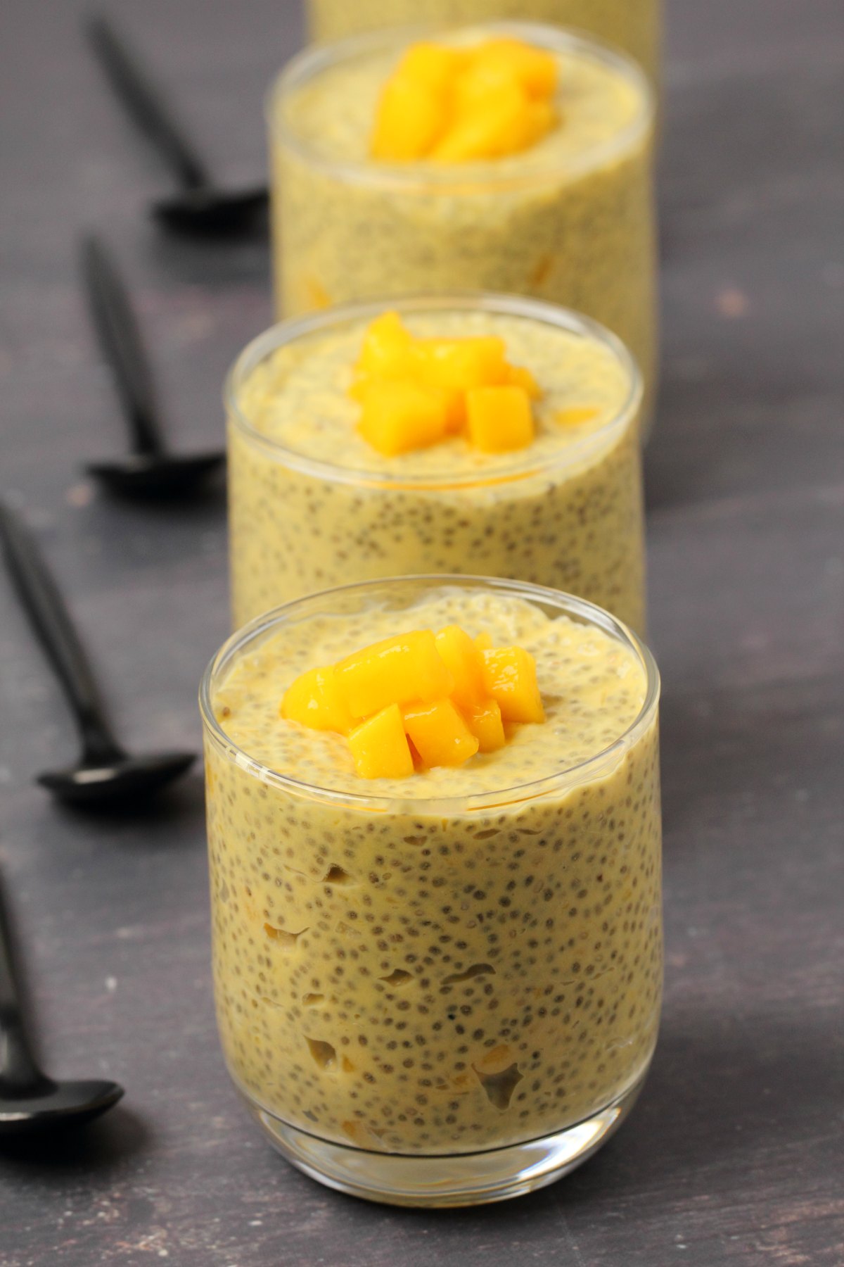 Mango chia pudding topped with mango chunks in glasses.