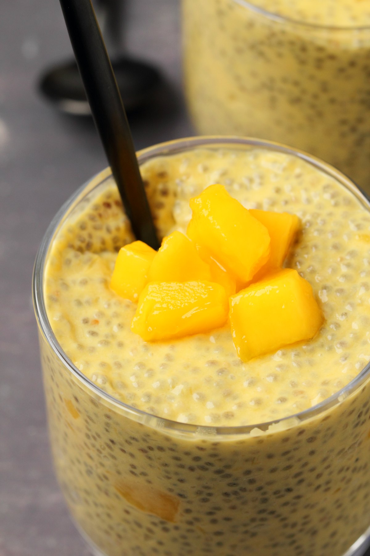Mango chia pudding topped with mango chunks in a glass with a spoon. 
