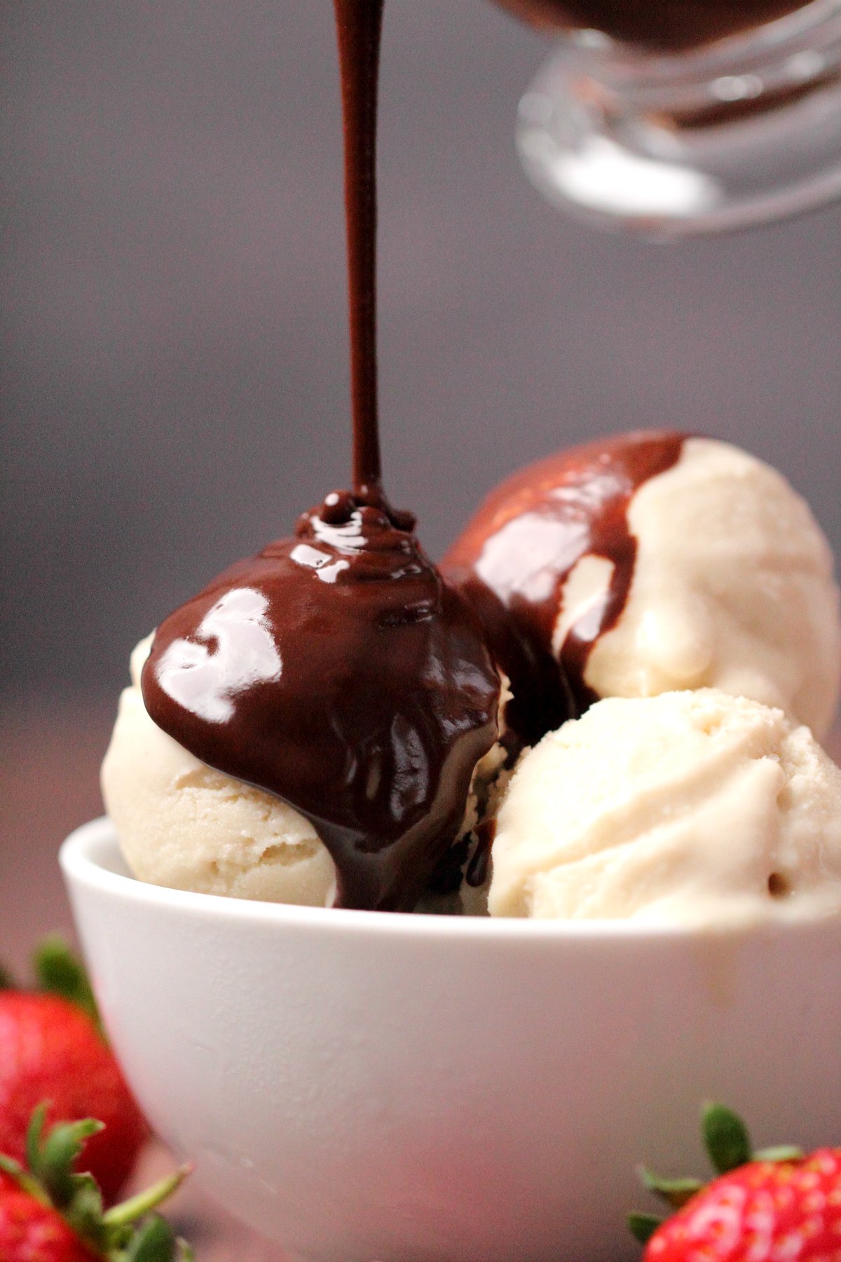 Chocolate sauce pouring over ice cream in a white bowl. 