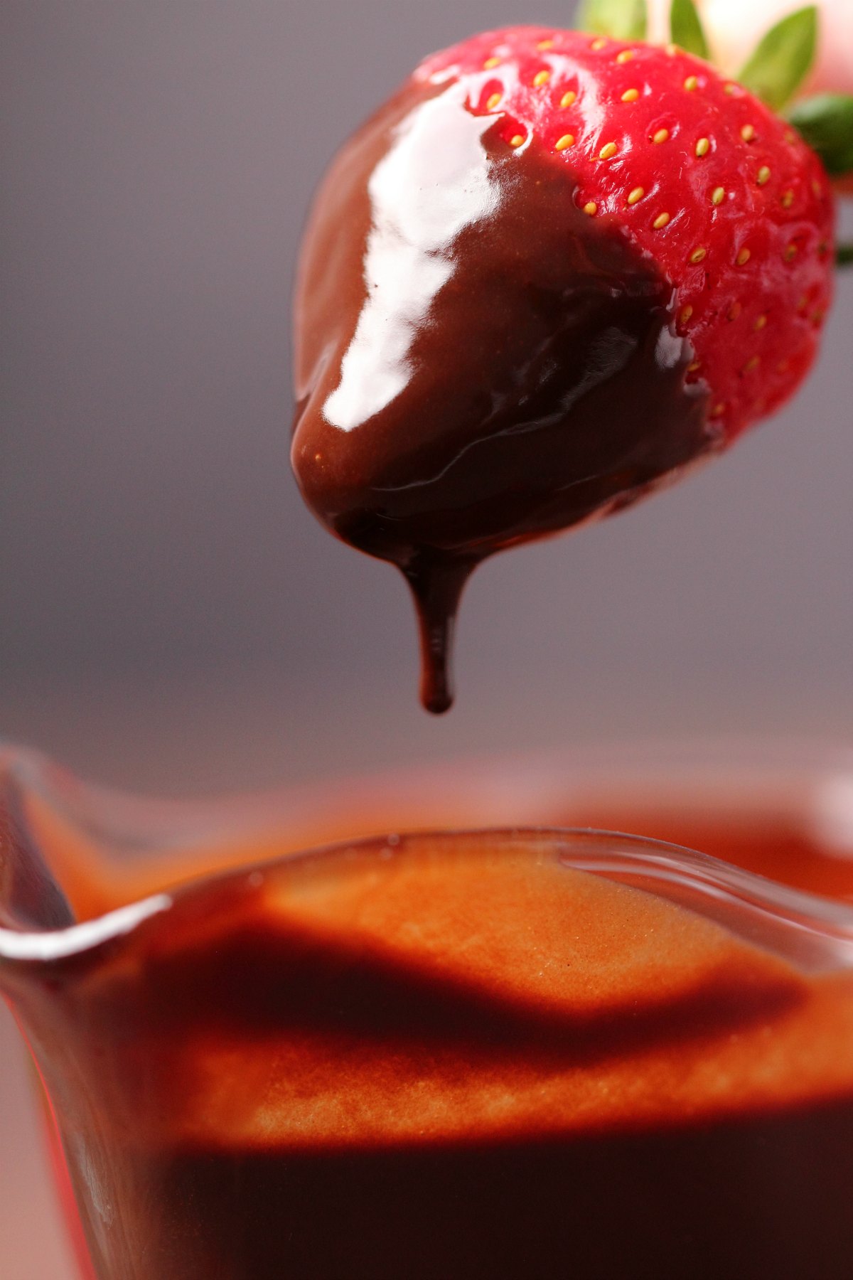 um morango mergulhando em molho de chocolate. 