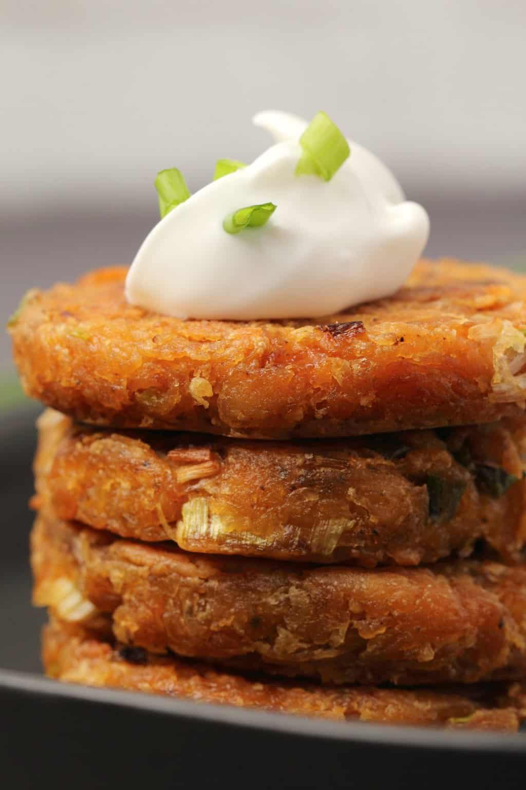 Stack of vegan hash browns topped with a dollop of vegan mayo and some chopped spring onions. 