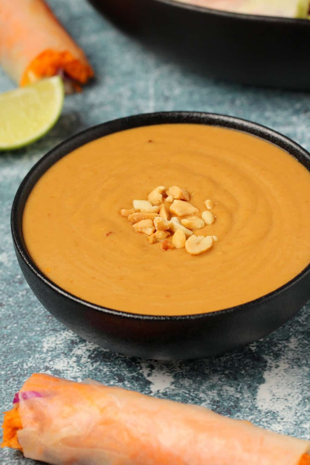 Vegan peanut sauce topped with crushed peanuts in a black bowl. 