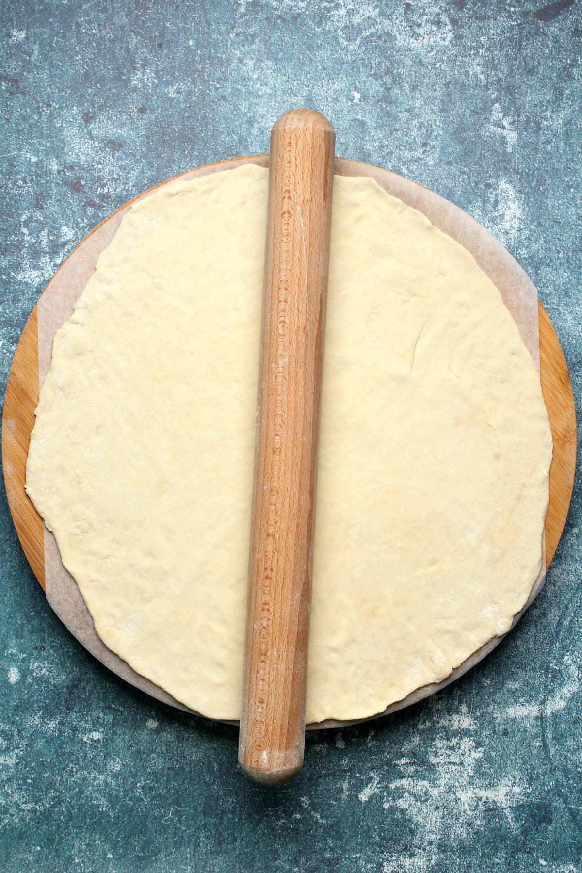 Rolled out pizza dough on parchment paper with a rolling pin.