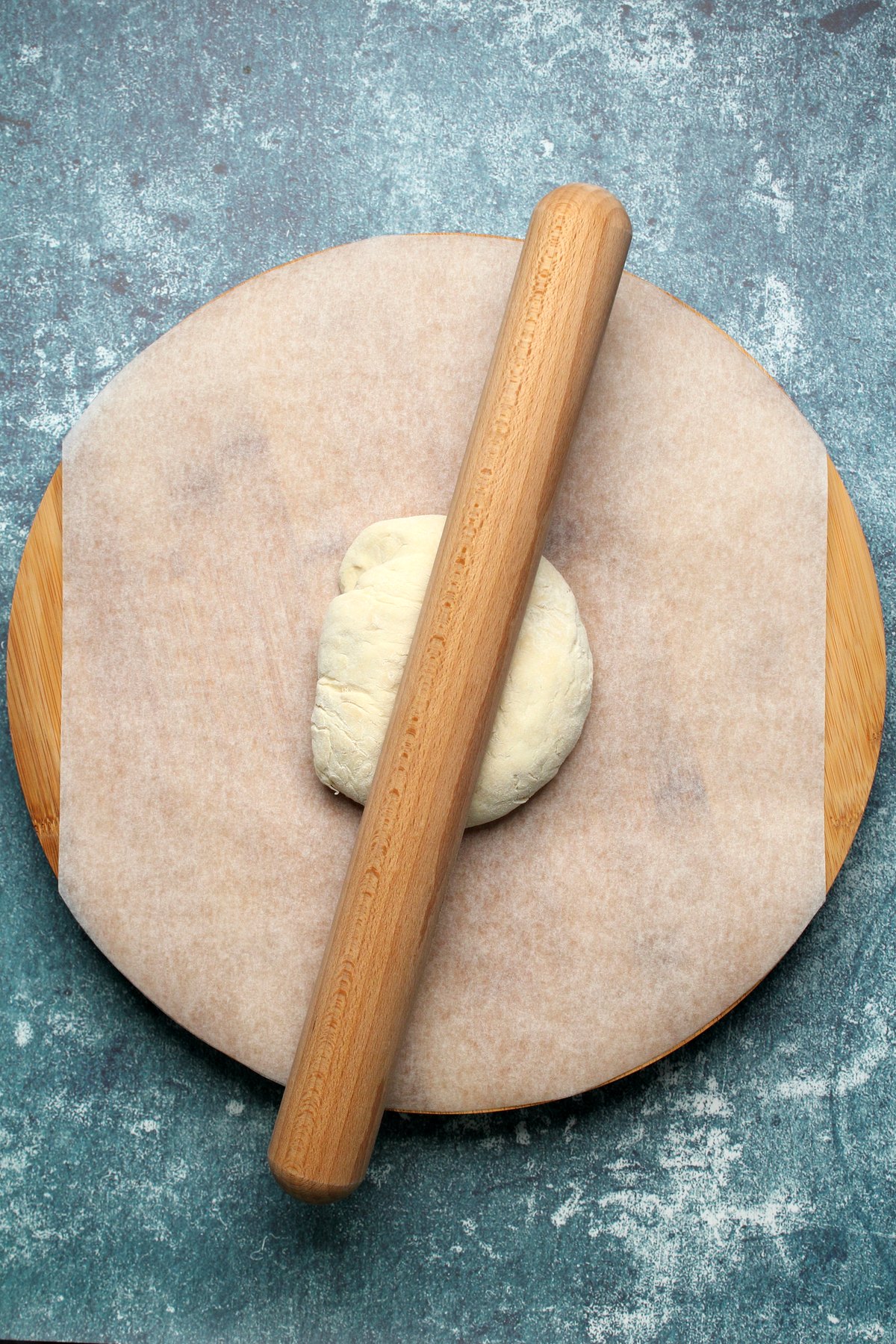 Ball of dough on parchment paper with a rolling pin.