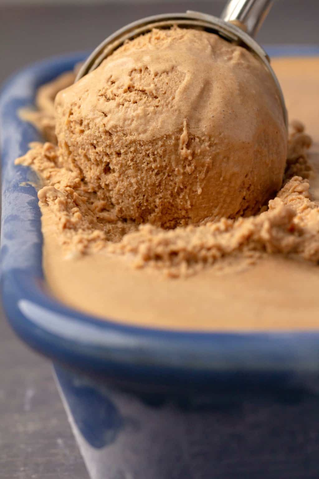 Vegan coffee ice cream in a blue ceramic dish with an ice cream scoop. 