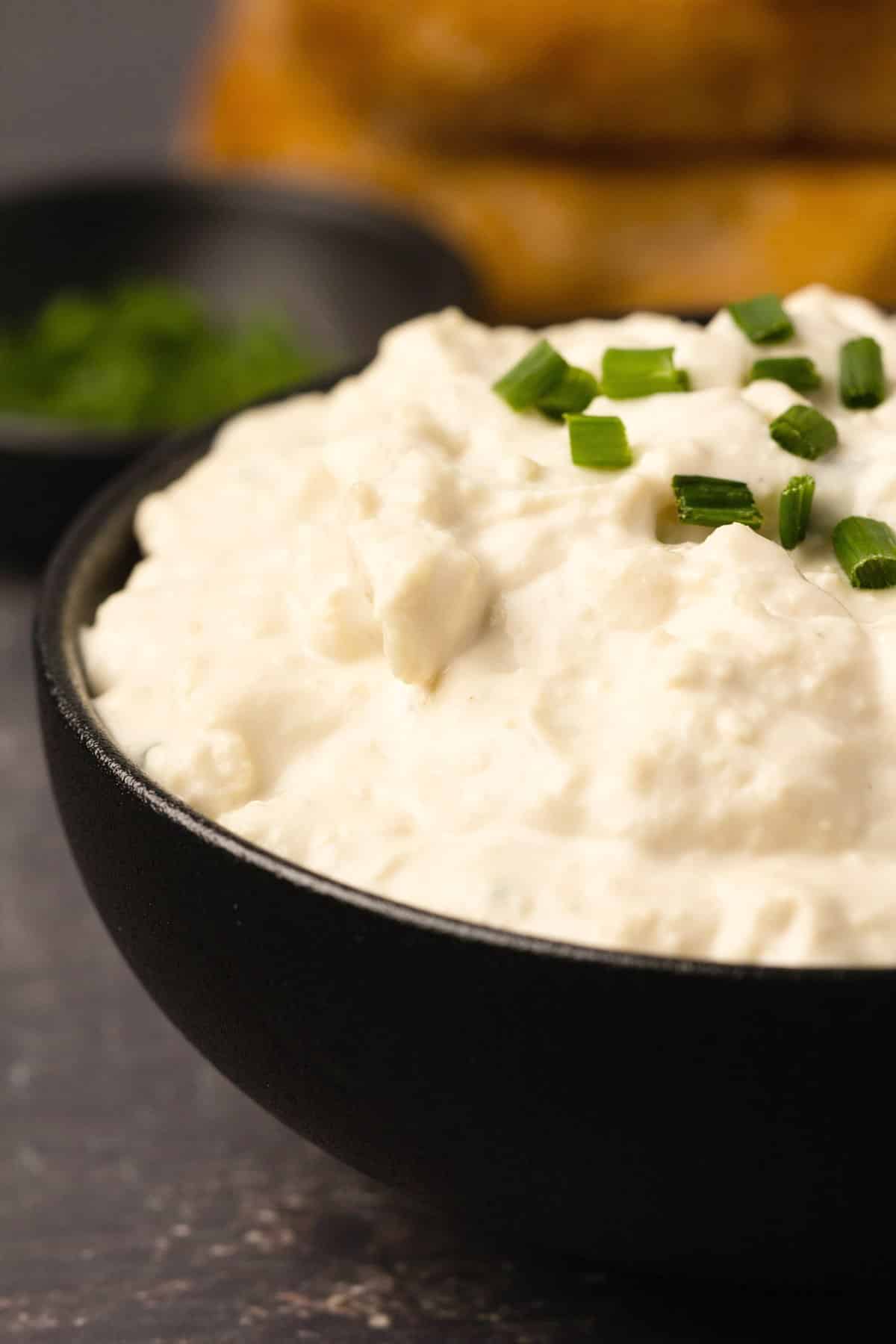 Vegan cottage cheese with chopped chives in a black bowl. 