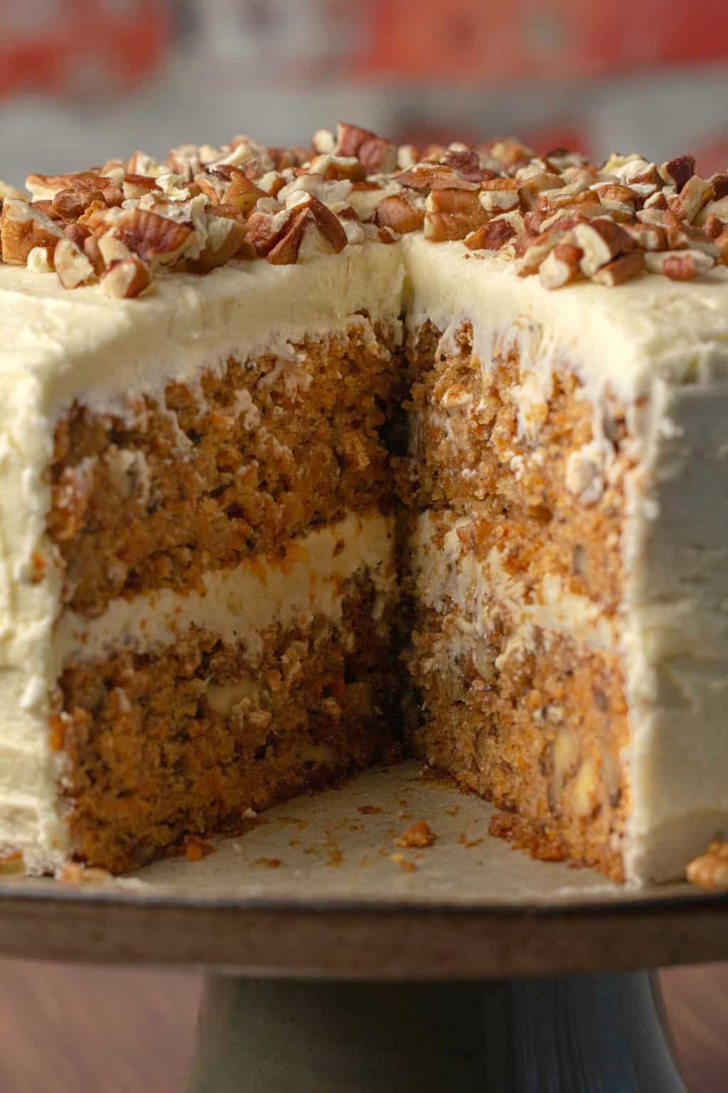 Vegan gluten free carrot cake with a slice removed on a cake stand.